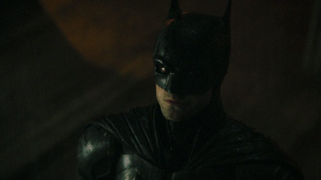 Batman enveloped in shadow, eyeing the Bat Signal off-screen in the sky