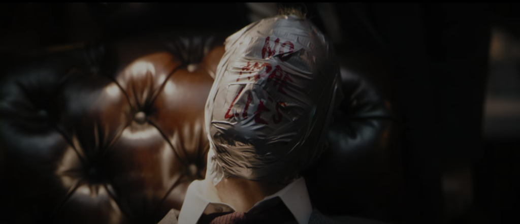 The Riddler's first victim, head encased in duct tape with "No More Lies" scrawled across his face.